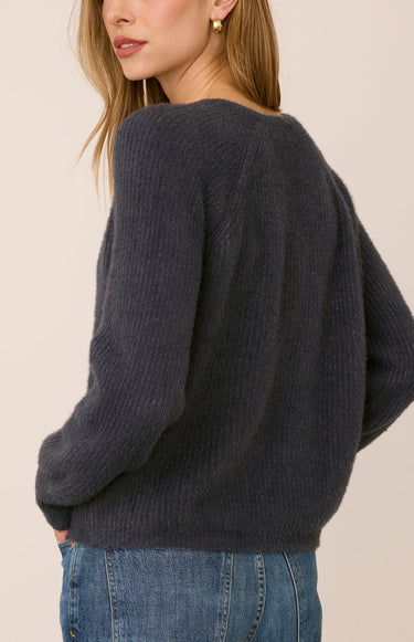 A woman facing backwards wearing a gray ribbed sweater and jeans on a white background