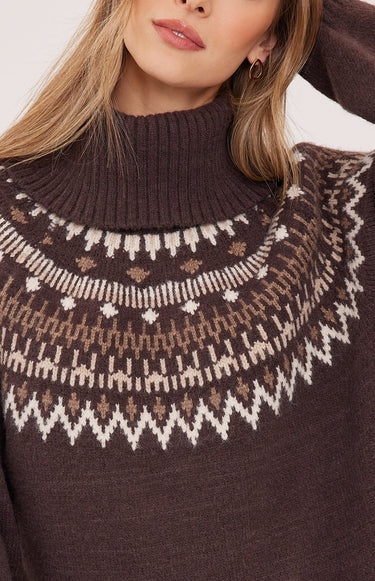 A woman wearing in a brown turtle neck with a fair isle print on white background.