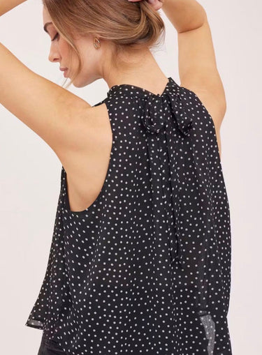 A woman wearing a black sleeveless top with a white polka dot pattern, shown from the back against a light beige studio background.