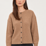 A woman wearing a cropped, long-sleeve knit cardigan in a warm camel brown color with dark buttons, paired with black jeans, against a plain light background.