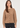 A woman wearing a cropped, long-sleeve knit cardigan in a warm camel brown color with dark buttons, paired with black jeans, against a plain light background.