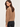 A woman wearing a textured knit sweater in a warm camel brown color, paired with black jeans, photographed against a clean off-white studio background.