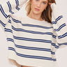 A woman wearing a cream and navy stripe oversized sweater and blue jeans on a white background
