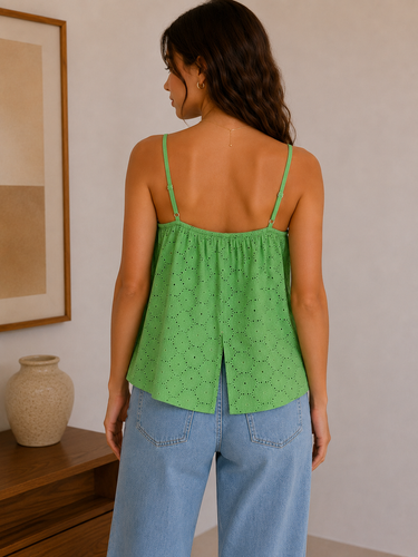 Woman wearing a green top and blue jeans in a room with a vase and framed picture.