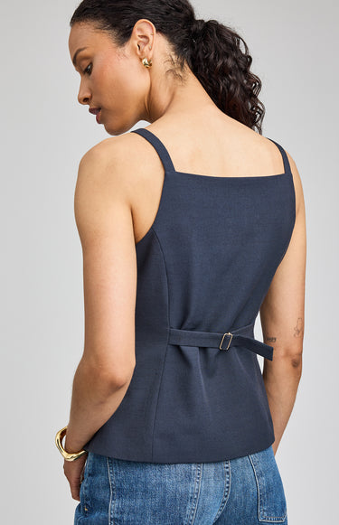Woman wearing a navy blue sleeveless top with a belt, standing against a gray background