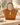 Camel suede handbag with gold hardware shown from a front  angle on a neutral travertine table.