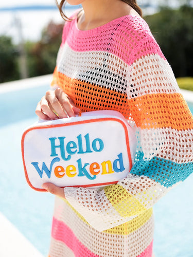 Person holding a 'Hello Weekend' pouch by a poolside
