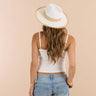 Person wearing a white tank top, blue jeans, and a white sun hat on a beige background