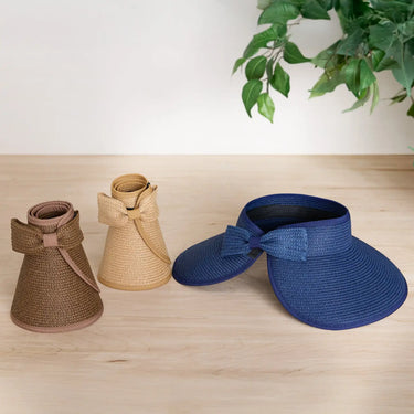 Two straw visors, one brown and one blue, on a wooden surface with a plant in the background.