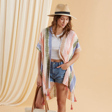Woman wearing a colorful kimono-style garment and straw hat against a beige curtain.