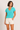 Woman wearing a turquoise top and white shorts on a plain background
