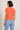 Woman wearing a coral t-shirt and blue jeans on a plain background