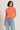 Woman wearing a coral top and blue jeans on a beige background