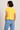 Woman wearing a yellow t-shirt and blue jeans against a plain background