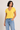 Woman wearing a yellow top and blue jeans against a plain background