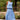 Woman wearing a blue tank and skirt standing outdoors with greenery and flowers in the background