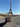 A cosmetic zipper pouch in black with world landmark pictures printed onto it being held in front of the Eiffel Tower 