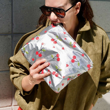 a woman holding the medium metallic zippered pouch with cherries and biting it