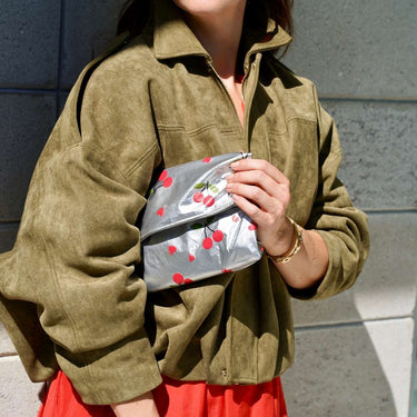 a woman holding the folded medium zippered metallic cherries pouch under her arm