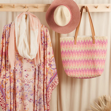 Colorful scarf, straw hat, and patterned bag hanging on a wooden rack against a beige wall.