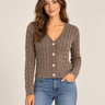 A woman wearing an acid wash cable knit cardigan in chocolate with blue jeans on a neutral background
