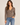 A woman wearing an acid wash cable knit cardigan in chocolate with blue jeans on a neutral background