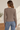 A woman wearing an acid wash cable knit cardigan in chocolate with blue jeans on a neutral background