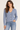 A woman wearing an acid wash cable knit cardigan in denim blue with blue jeans on a white background
