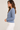 A woman wearing an acid wash cable knit cardigan in denim blue with blue jeans on a white background