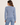 A woman facing backwards wearing an acid wash cable knit cardigan in denim blue with blue jeans on a white background