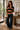 A woman stands indoors wearing a long-sleeve striped knit sweater with dark blue wide-leg jeans and brown flats. The sweater has horizontal stripes in tan and dark navy, with a dark navy collar and placket.