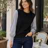a woman wearing a black crew neck with black and white polo stripe sleeves and blue jeans on neutral background.
