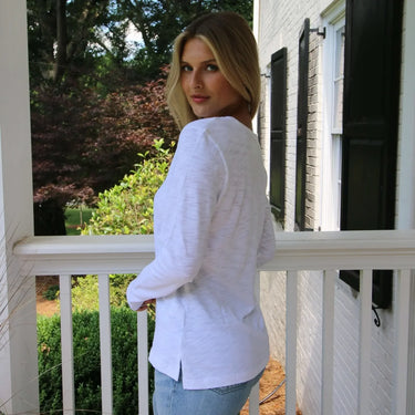 Woman in a white sweater standing on a porch with a house and garden in the background
