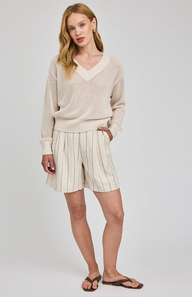 Woman wearing a beige sweater and striped shorts on a plain background