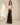 A woman stands in profile wearing a cream ribbed tank top and high-waisted, wide-leg black pants against a warm beige textured studio wall.