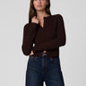 a woman wearing a dark brown cardigan and dark blue jeans on a white background