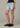 Person wearing light blue denim shorts and black shoes on a neutral background