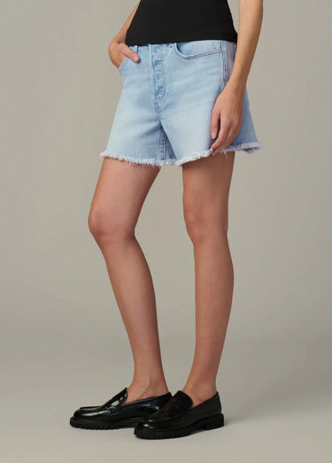 Person wearing light blue denim shorts and black shoes on a neutral background