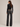 A woman shown from the back wearing a black long-sleeve crop top and dark gray wide-leg jeans against a plain light gray studio background.