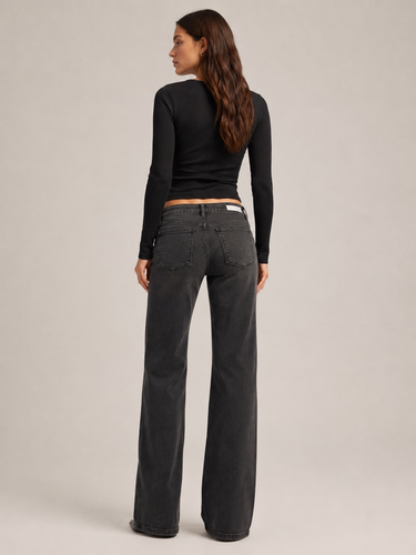 A woman shown from the back wearing a black long-sleeve crop top and dark gray wide-leg jeans against a plain light gray studio background.