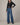 Woman wearing a black long-sleeve top and blue jeans on a neutral background