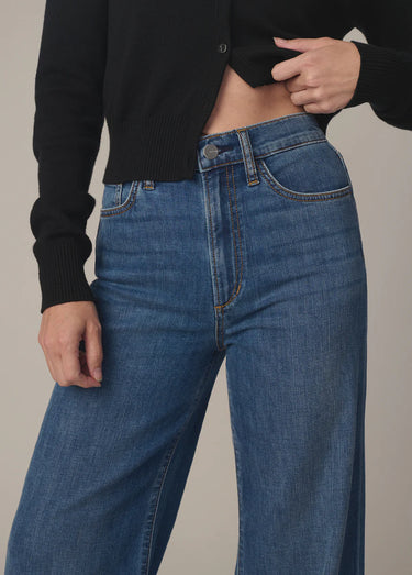 Person wearing blue jeans and a black cropped sweater on a neutral background