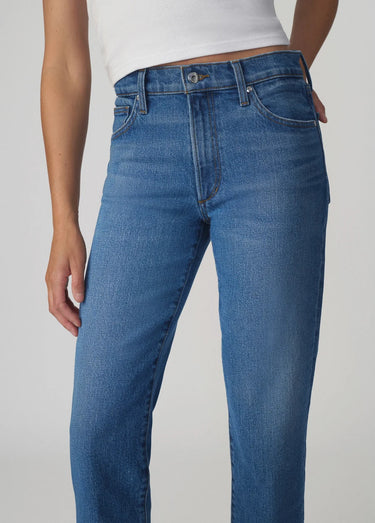 Mid-rise ankle length Blue jeans worn by a person on a plain background