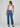 A woman is shown from the back wearing a white ribbed tank top and Mid-rise-waisted, wide-leg blue denim jeans with dark brown sandals, set against a plain light gray studio background.