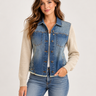 a woman wearing a denim jacket with grey knit sleeves and blue jeans on a white background.
