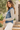a woman wearing a denim jacket with grey knit sleeves and white jeans on a outdoor background.