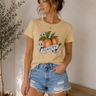 Woman wearing a yellow t-shirt with a peach graphic and 'Peachy' text, standing indoors.