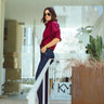 Woman in a red blouse and blue jeans standing in a modern indoor setting with plants and boxes.