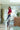 Woman in a red blouse and blue jeans standing in a modern indoor setting with plants and boxes.
