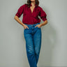Woman wearing a red blouse and blue jeans against a plain background